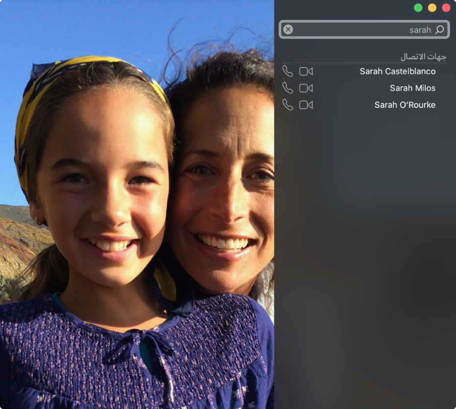 نافذة FaceTime قبل إجراء مكالمة. يوجد أعلى اليسار حقل بحث، مع إدخال الاسم "سارة" في الحقل، وبالأسفل توجد قائمة بنتائج البحث تعرض جهات الاتصال بالاسم "سارة"، مع أزرار بجوار كل جهة اتصال تتيح لك بدء مكالمة فيديو أو مكالمة صوتية. يوجد على اليمين ما تعرضه الكاميرا الخاصة بك-شخصان مستعدان لإجراء مكالمة.