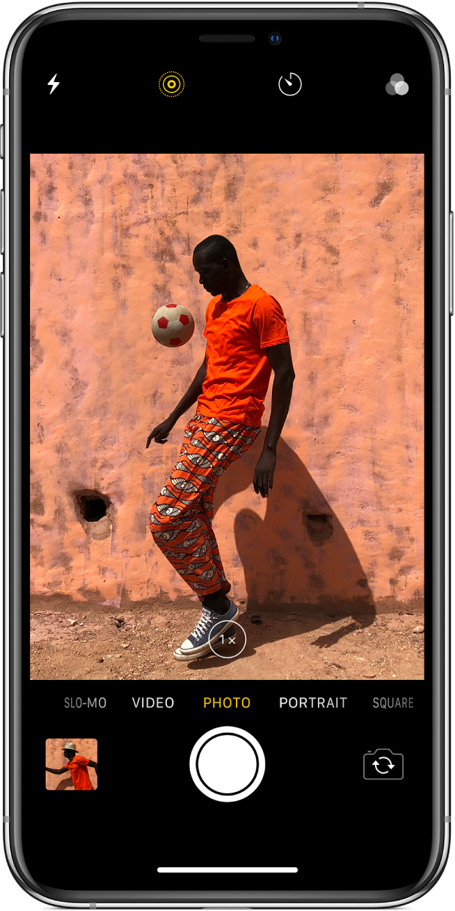 Camera screen in Photo mode, with other modes to the left and right below the viewer. Buttons for Flash, Live Photo, Timer, and Filters appear at the top of the screen. An image thumbnail at the lower left gives access to view existing photos and videos. The Shutter button is at the bottom center, and the Switch Camera button is in the lower right.