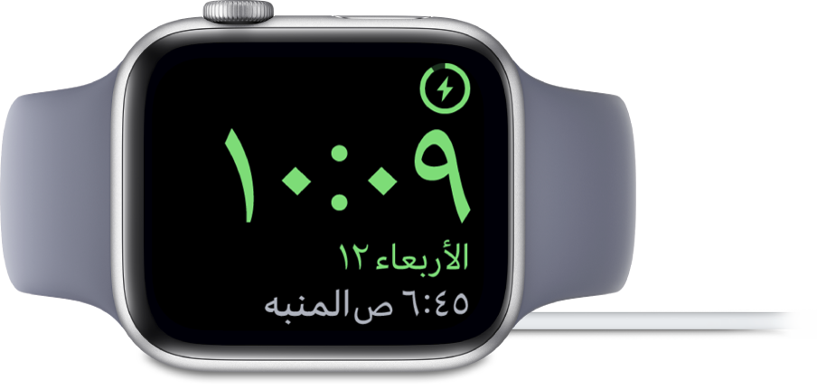 Apple Watch موضوعة على جانبها ومتصلة بالشاحن، وتعرض الشاشة رمز الشحن في الزاوية العلوية اليمنى، والوقت الحالي أسفل ذلك، ووقت المنبه التالي.