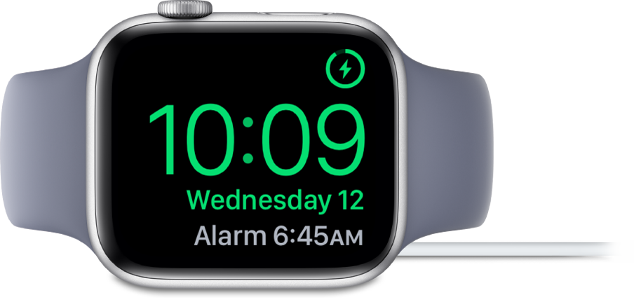 Küljele asetatud ja laadijaga ühendatud Apple Watch, mille ekraanil kuvatakse ülemises paremas nurgas laadimissümbolit, selle all praegust kellaaega ning järgmise äratuse kellaaega.
