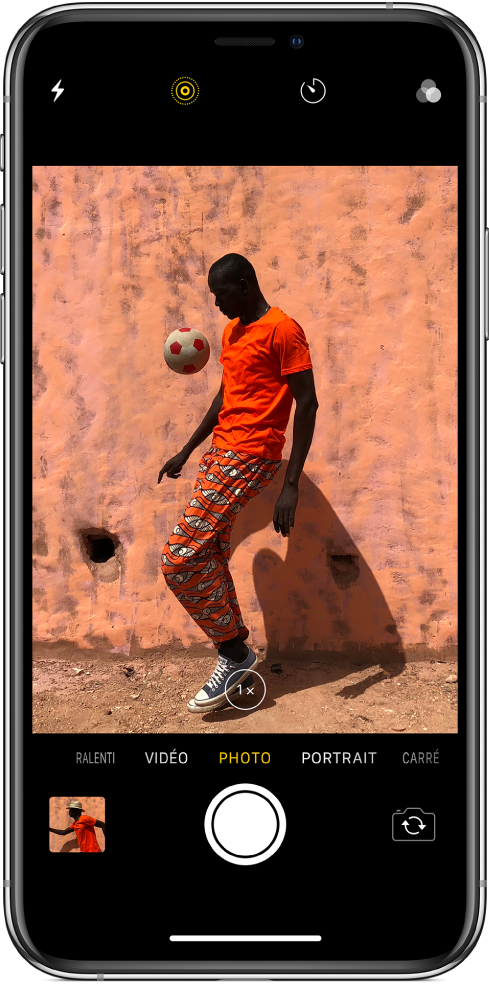 L’écran Appareil photo en mode Photo, avec les autres modes à gauche et à droite sous le visualiseur. Les boutons pour le flash, le mode Live Photo, le retardateur et les filtres apparaissent en haut de l’écran. Touchez la vignette située en bas à gauche pour accéder aux photos et aux vidéos existantes. Le bouton de l’obturateur se trouve en bas au centre et le bouton Changer de caméra est dans le coin inférieur droit.