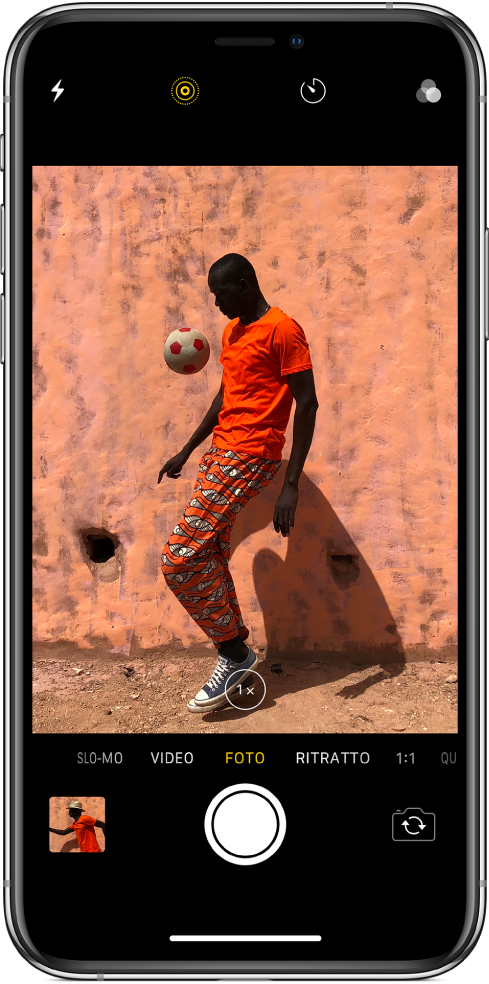 Schermata di Fotocamera in modalità Foto, con altre modalità a sinistra e a destra sotto il visore. Pulsanti per Flash, Live Photo, Timer e Filtri mostrati nella parte alta dello schermo. In basso a sinistra, una miniatura dell'immagine ti consente di visualizzare le foto e i video esistenti. Il pulsante Otturatore è posizionato in basso al centro e il pulsante “Cambia fotocamera” si trova in basso a destra.