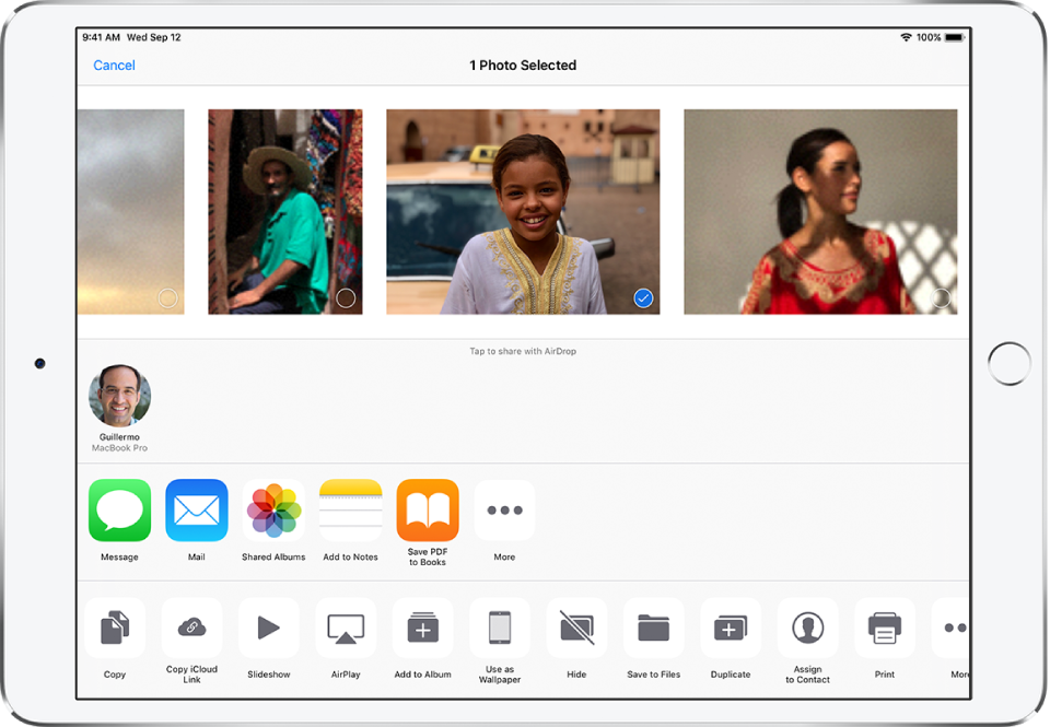 The Sharing screen with photos across the top; one photo is selected, indicated with a white checkmark in a blue circle. The row beneath the photos shows friends you can share with using AirDrop. Below that are other sharing options, including, from left to right, Messages, Mail, Shared Albums, Add to Notes, Save PDF to Books, and More. In the bottom row are the Copy, Save to Files, Copy iCloud Link, Slideshow, AirPlay, Add to Album, Use as Wallpaper, Hide, Duplicate, Assign to Contact, Print, and More buttons.