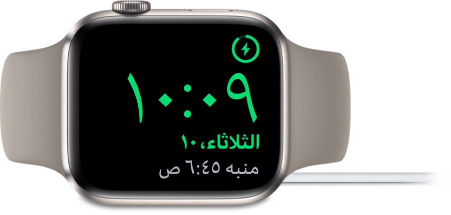 Apple Watch موضوعة على جانبها ومتصلة بالشاحن، وتعرض الشاشة رمز الشحن في الزاوية العلوية اليمنى، والوقت الحالي أسفل ذلك، ووقت المنبه التالي.