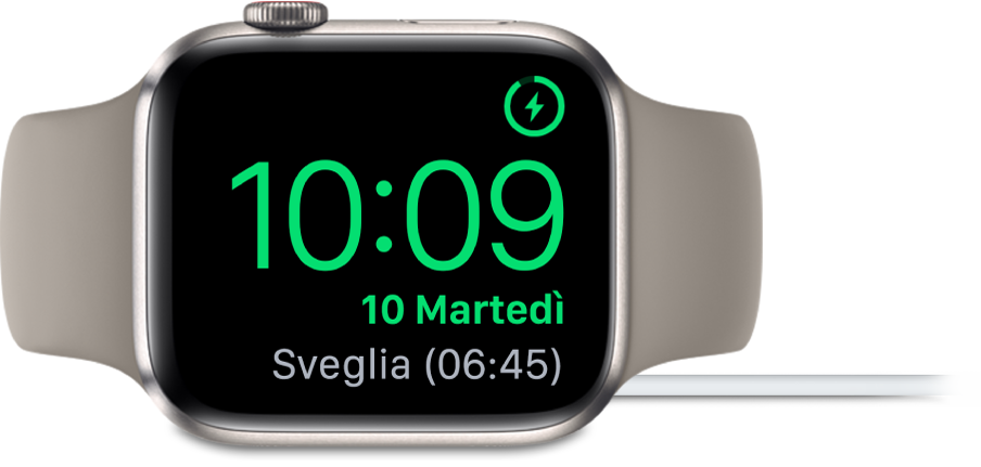 Apple Watch appoggiato su un lato e collegato al caricatore, con lo schermo che mostra il simbolo di ricarica nell’angolo superiore destro, l’ora attuale sotto e l'orario della prossima sveglia.