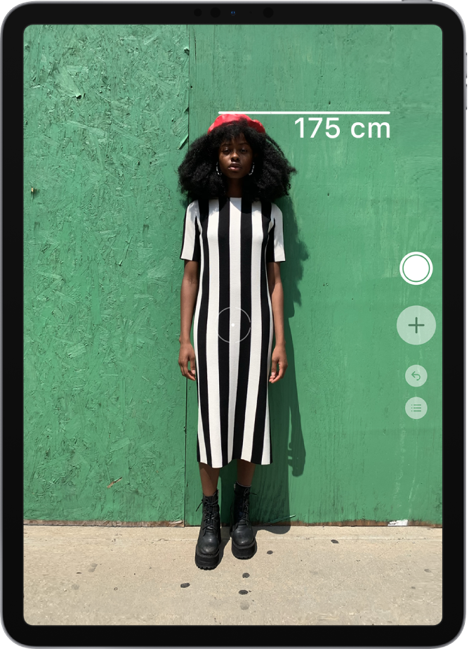 La taille d’une personne est en cours de mesure, avec la mesure de la taille affichée en haut de la tête de la personne. Le bouton « Prendre une photo » est actif sur le bord droit pour prendre une photo de la mesure.