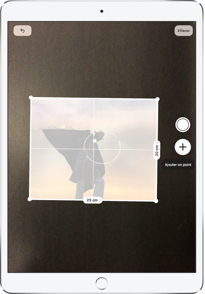 Une photographie papier est mesurée et ses dimensions s’affichent le long de ses bords droit et inférieur. Le bouton Prendre une photo est situé vers le milieu du bord droit. L’indicateur vert « Caméra en cours d’utilisation » apparaît en haut à droite.