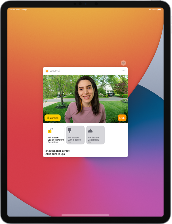 O notificare din aplicația Locuință este afișată pe ecranul iPad-ului. Aceasta prezintă poza unei persoane care este la ușa din față și butonul Vorbire în stânga. Dedesubt se află butoanele accesoriilor pentru ușa din față și luminile de la intrare. Adresa locuinței se află în partea de jos, alături de cuvintele “Alina sună la ușă”. Butonul Închideți se află în partea dreaptă sus a notificării.