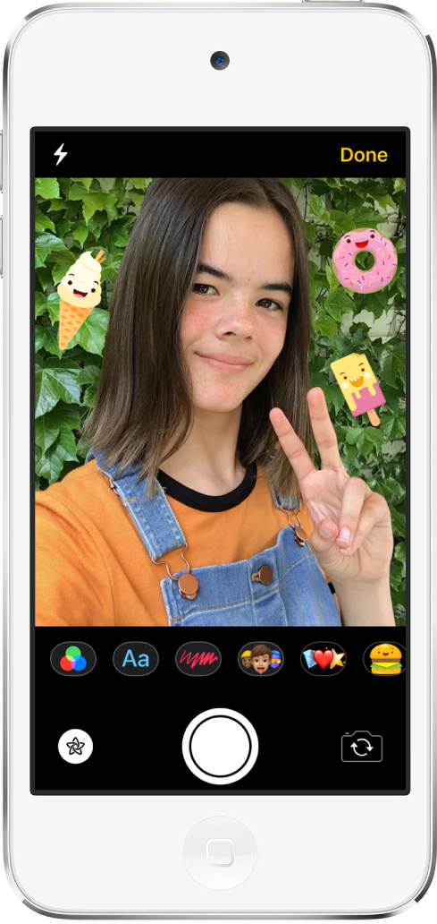The Messages effects screen. The top of the screen shows the front camera frame. iMessage stickers are around the subject in the frame. Below the frame, from left to right, are the filters, text, shapes, Memoji, Animoji, and iMessage app buttons. At the bottom of the screen, from left to right, are the Effects, Shutter, and Camera Chooser buttons.