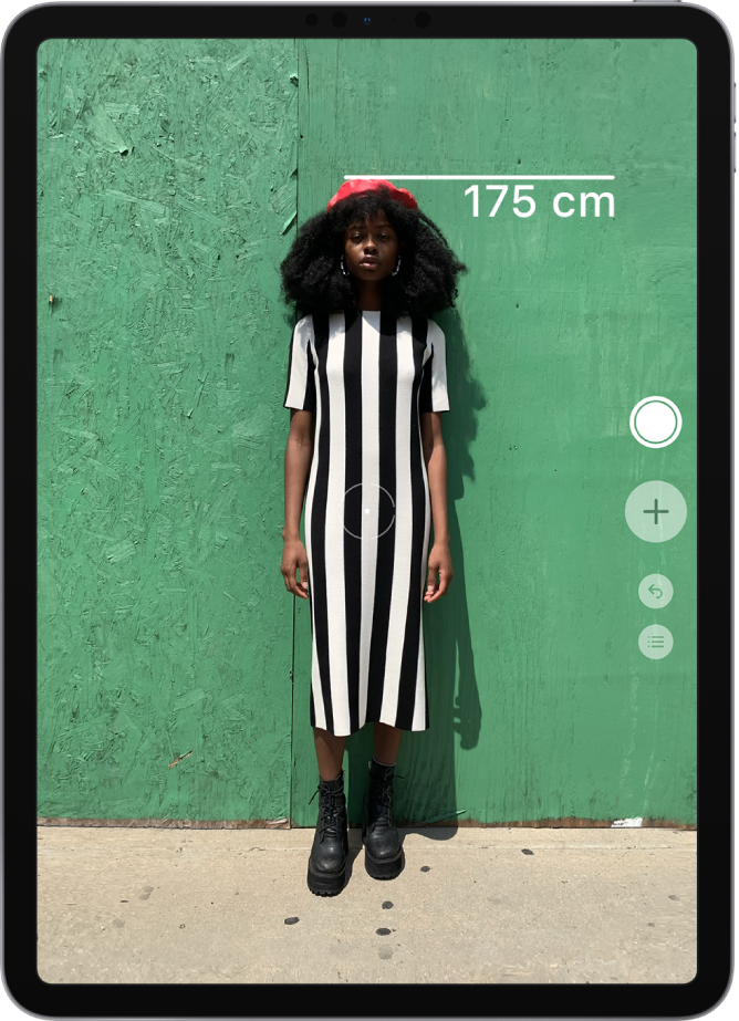 Iemands lengte wordt gemeten, waarbij de lengte boven het hoofd wordt weergegeven. De knop 'Maak foto' is actief aan de rechterkant, zodat je een foto van de meting kunt maken.