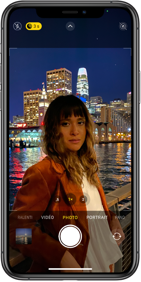 L’écran de l’appareil photo en mode Photo. Les boutons correspondant au flash et au mode Nuit s’affichent dans l’angle supérieur gauche de l’écran. Le flash est désactivé et le mode Nuit est actif. Le bouton « Commandes de l’appareil photo » se trouve en haut au centre et le bouton « Live Photo » dans le coin supérieur droit. En bas de l’écran, de gauche à droite, se trouvent le bouton « Visualiseur de photos et vidéos », le bouton « Prendre une photo » et le bouton « Sélecteur de caméra - face arrière ».