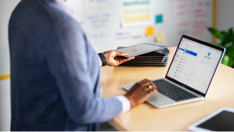 Une femme à son bureau, travaillant sur un ordinateur portable Mac, avec une pile d’iPad à proximité.