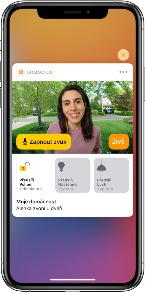 Oznámení od aplikace Domácnost na displeji iPhonu. Zobrazuje se na něm snímek člověka u vstupních dveří s tlačítkem „Zapnout zvuk“ po levé straně. Pod ním se nacházejí tlačítka příslušenství pro osvětlení vstupních dveří a předsíně. Pod tlačítky příslušenství je napsáno: „Alenka zvoní u dveří.“ V pravém horním rohu oznámení se nachází tlačítko Zavřít.