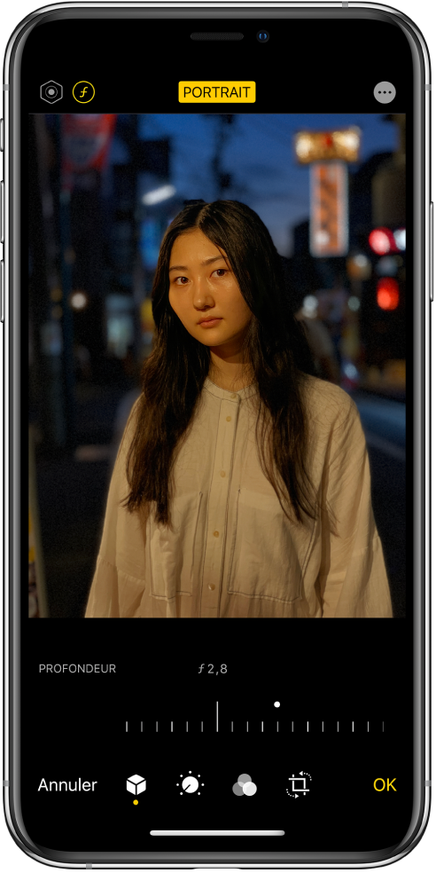 L’écran Modifier d’une photo prise en mode Portrait. En haut à gauche de l’écran se trouvent les boutons « Intensité de l’éclairage » et « Réglage de la profondeur ». En haut, au centre de l’écran, le bouton Portrait est activé et en haut à droite se trouve le bouton Modules. La photo est au centre de l’écran ; sous celle-ci se trouve un curseur permettant d’ajuster le réglage de la profondeur. Sous ce curseur se trouvent, de gauche à droite, les boutons Annuler, Portrait, Ajuster, Filtres, Recadrer et OK.