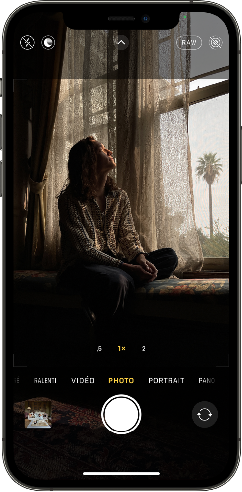 L’écran « Appareil photo » en mode Photo. Les boutons correspondant au flash et au mode Nuit s’affichent dans l’angle supérieur gauche de l’écran. Le bouton Flash et le bouton du mode Nuit sont désactivés. Le bouton « Commandes de l’appareil photo » se trouve en haut au centre et les boutons ProRAW et « Live Photo » se trouvent dans le coin supérieur droit. Le bouton ProRAW est activé et le bouton « Live Photo » est désactivé. En bas de l’écran, de gauche à droite, se trouvent le bouton « Visualiseur de photos et vidéos », le bouton « Prendre une photo » et le bouton « Sélecteur de caméra - face arrière ».