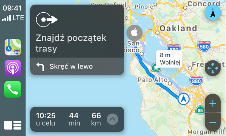 CarPlay z ikonami aplikacji Mapy, Podcasty i Telefon po lewej. Po prawej znajduje się mapa trasy przejazdu, zawierająca elementy sterujące do powiększania i pomniejszania, wskazówki krok po kroku oraz szacowany czas przybycia do celu.