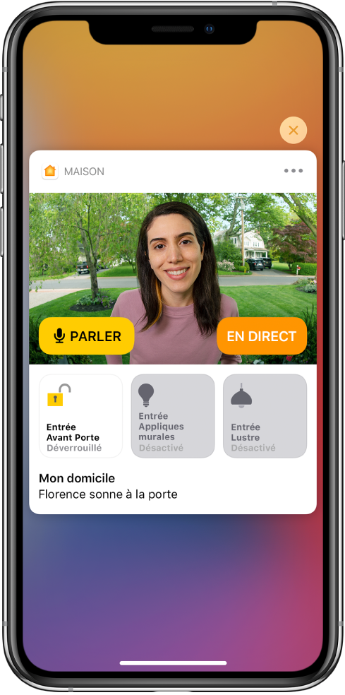 Une notification de Maison est affichée sur l’écran de l’iPhone. Elle montre la photo d’une personne à la porte d’entrée avec un bouton Parler sur la gauche. Des boutons d’accessoires pour les lumières de la porte d’entrée et de l’entrée se trouvent en dessous, avec les mots « Ashley sonne à la porte ». Un bouton Fermer apparaît en haut à droite de la notification.