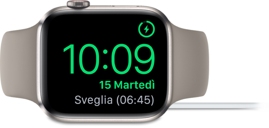 Apple Watch appoggiato su un lato e collegato al caricatore, con lo schermo che mostra il simbolo di ricarica nell’angolo superiore destro, l’ora attuale sotto e l'orario della prossima sveglia.