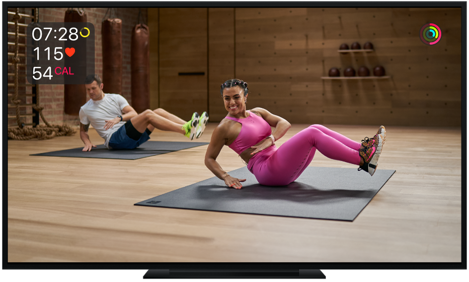 Televizorius, kuriame rodoma „Apple Fitness+“ pagrindinė treniruotė. Ekrane rodomas likęs laikas, pulso dažnis ir kalorijos.