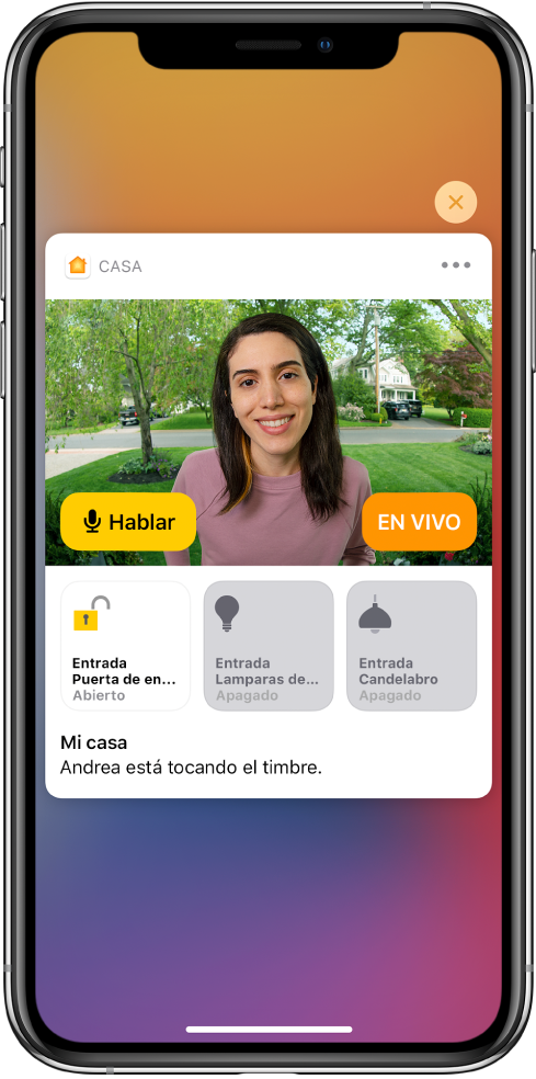 Se muestra una notificación de Casa en la pantalla del iPhone. Muestra una foto de una persona en la puerta principal con el botón Hablar a la izquierda. En la parte inferior hay botones de accesorios de las luces de la puerta principal y la entrada. Las palabras “Andrea está tocando el timbre” aparecen debajo de los botones del accesorio. El botón Cerrar aparece en la parte superior derecha de la notificación.