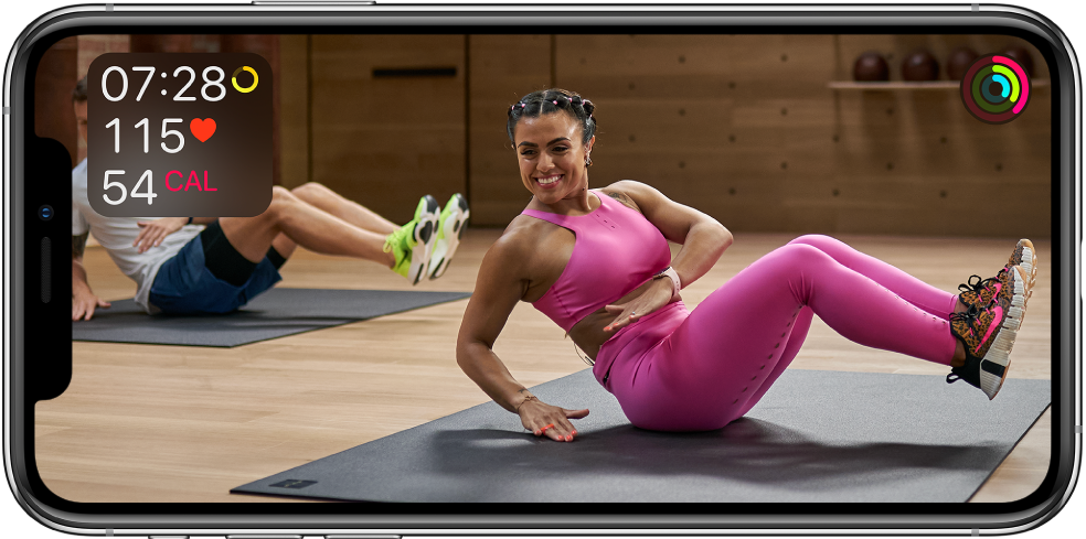 トレーナーが指導するApple Fitness+のワークアウトが表示されている画面。左上にワークアウトの時間、心拍数、および消費カロリーが表示されます。右上にムーブ、エクササイズ、スタンドゴールのリングの進捗が表示されます。