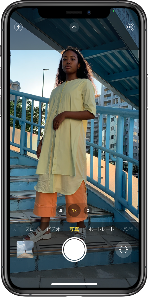 写真モードの「カメラ」。ビューファインダーの下に、その他のモードが左右に表示されています。画面上部には、フラッシュ、カメラコントロール、Live Photosの各ボタンがあります。左下隅には写真およびビデオビューアボタンがあります。下部中央には写真撮影ボタン、右下隅には背面側カメラ選択ボタンがあります。