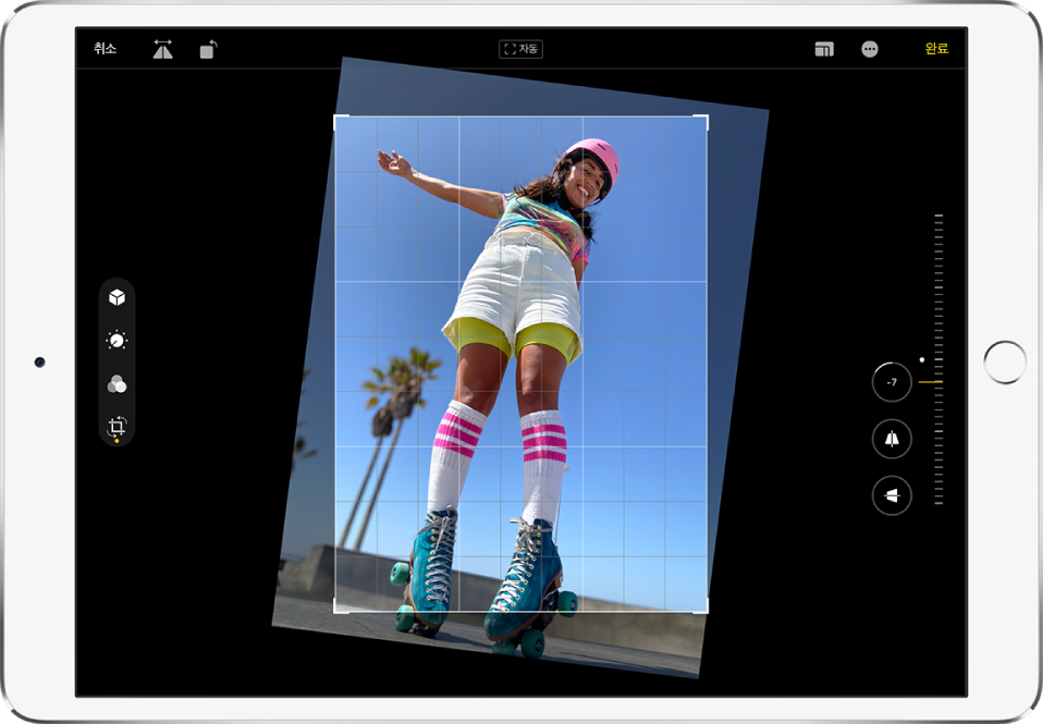 가로 화면 방향의 iPad. 화면 중앙에는 격자 오버레이 및 자르기 프레임이 있는 편집 모드 상태의 사진이 있음. 화면 왼쪽에 자르기 버튼이 선택됨. 화면 오른쪽에 배치 향상 옵션이 있음. 수평 맞추기가 선택되어 있고 강도 슬라이더가 -5로 조절되어 있음.