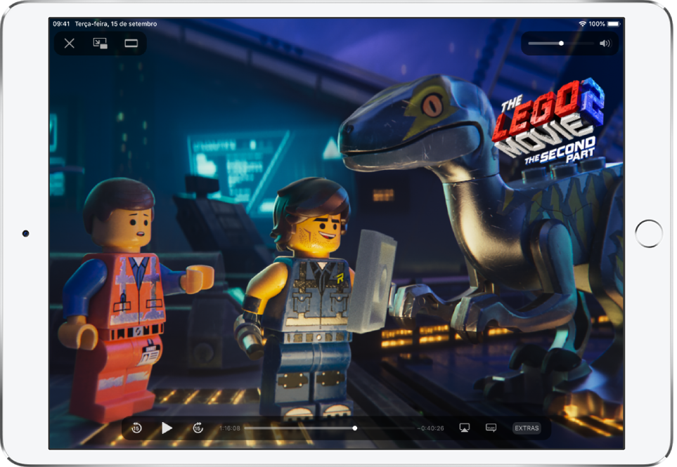 Filme sendo reproduzido, com controles de reprodução sendo exibidos. Os botões OK e Ajustar para Preencher se encontram na parte superior esquerda. O controle deslizante de volume se encontra na parte superior direita. Na parte inferior esquerda, os botões para retroceder 15 segundos, pausar e avançar 15 segundos. Ao longo da parte inferior central, um controle deslizante que pode ser arrastado para ajustar a posição do vídeo; o tempo decorrido e o tempo restante aparecem em cada um dos lados do controle deslizante. Na parte inferior direita, há botões para alterar o destino do vídeo, mostrar legendas e reproduzir conteúdo extra.