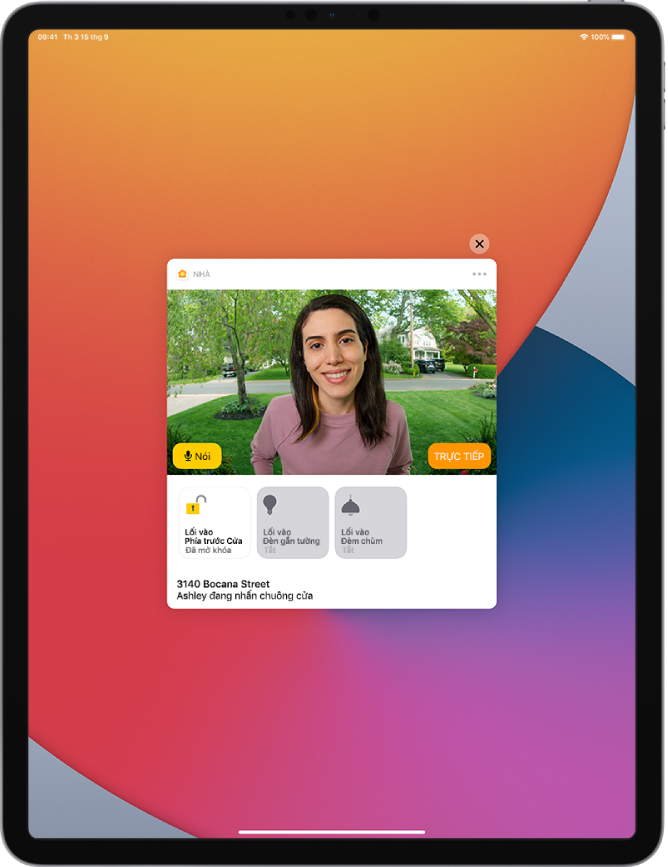 Một thông báo từ Nhà ở trên màn hình iPad. Thông báo hiển thị một hình ảnh về ngời ở cửa trước với nút Nói ở bên trái. Bên dưới là các nút phụ kiện cho cửa trước và đèn lối vào. Địa chỉ nhà ở dưới cùng với các từ “Ashley đang nhấn chuông cửa”. Nút Đóng ở trên cùng bên phải của thông báo.