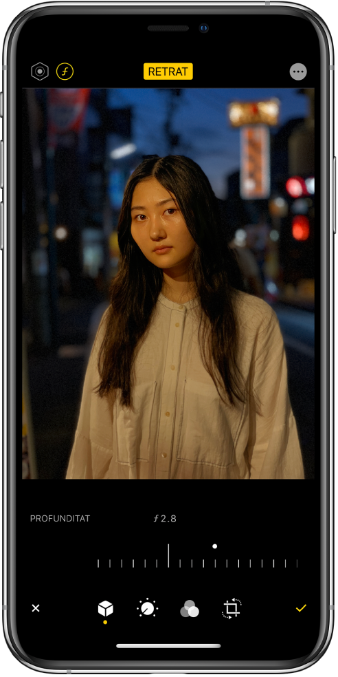 Pantalla Editar d’una foto en mode Retrat. A la part superior esquerra de la pantalla hi ha el botó d’intensitat de la il·luminació i d’ajustament de la profunditat. A la part superior central de la pantalla hi ha activat el botó Retrat, i a la part superior dreta hi ha el botó de connectors. La foto és al centre de la pantalla i a sota d’aquesta hi ha un regulador per ajustar la configuració d’“Ajustament de la profunditat”. A sota del regulador, d’esquerra a dreta, hi ha els botons Cancel·lar, Retrat, Ajustar, Retallar i Fet.