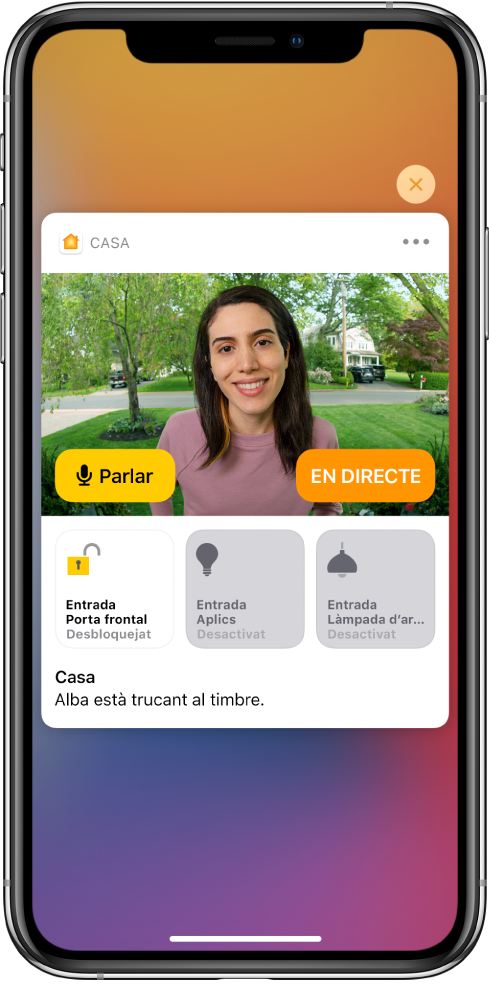 Notificació de l’app Casa a la pantalla de l’iPhone. Mostra una imatge d’una persona a la porta principal amb un botó per parlar a l’esquerra. A sota hi ha els botons dels accessoris per a la porta principal i els llums de l’accés d’entrada. Es mostren les paraules “La Laura està trucant al timbre” a sota dels botons dels accessoris. A l’angle superior dret de la notificació hi ha un botó per tancar.