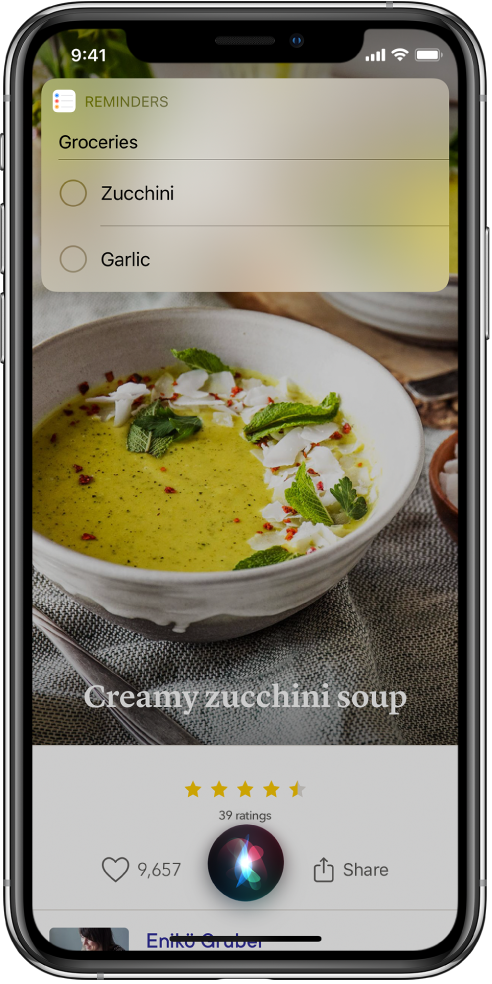 Siri reaguje na požadavek „Add zucchini and garlic to my groceries list“ zobrazením seznamu připomínek s názvem Potraviny, obsahujícím cukety a česnek. Pod seznamem je vidět recept na cuketový krém.