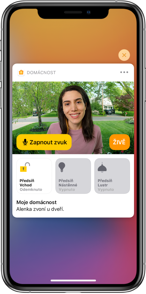 Oznámení od aplikace Domácnost na displeji iPhonu. Zobrazuje se na něm snímek člověka u vstupních dveří s tlačítkem „Zapnout zvuk“ po levé straně. Pod ním se nacházejí tlačítka příslušenství pro osvětlení vstupních dveří a předsíně. Pod tlačítky příslušenství je napsáno: „Alenka zvoní u dveří.“ V pravém horním rohu oznámení se nachází tlačítko Zavřít.