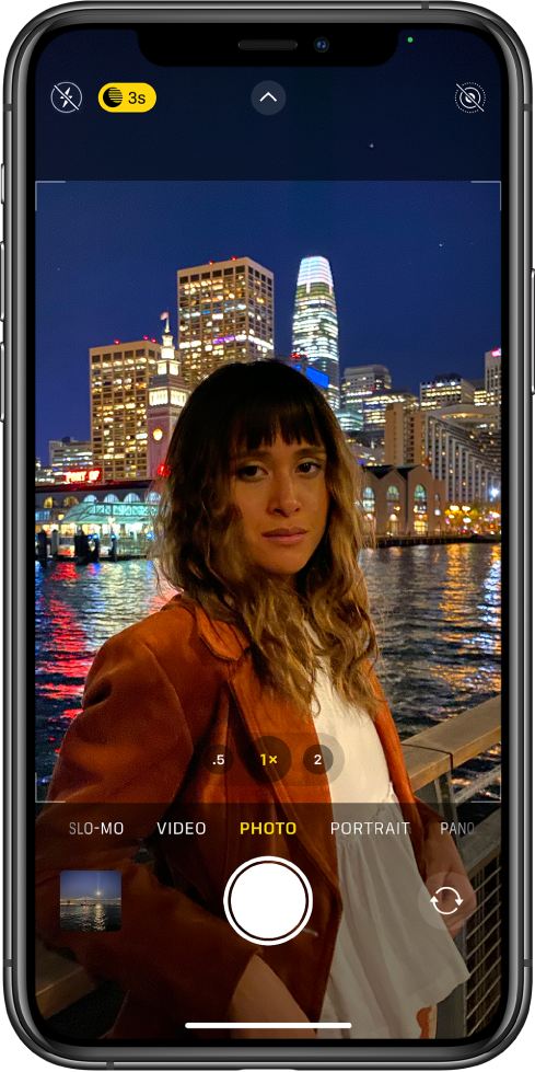 The Camera screen in Photo mode. Buttons for flash and Night mode appear in the top-left corner of the screen. The flash is turned off, and Night mode is on. The Camera Controls button is in top-center, and the Live Photo button is in the top-right corner. At the bottom of the screen are, from left to right, the Photo and Video Viewer button, the Take Picture button, and the Camera Chooser Back-Facing button.