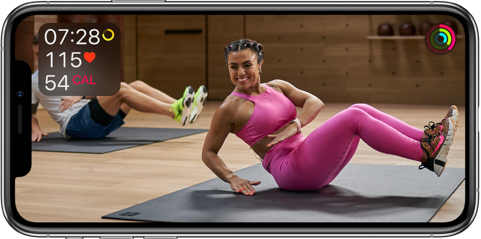 A screen showing a trainer leading an Apple Fitness Plus workout. Information about workout time, heart rate, and calories burned appears in the top left. Progress rings for move, exercise, and stand goals appear at the top right.