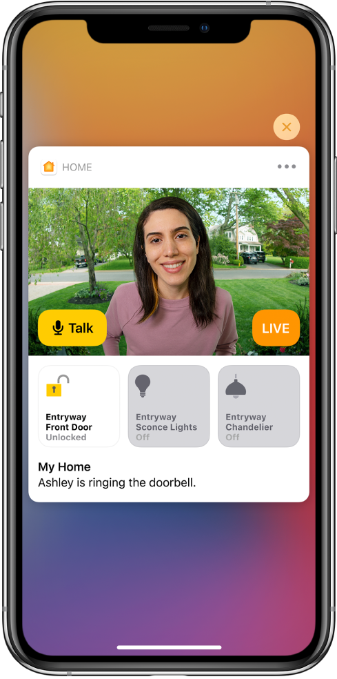 A notification from Home on the iPhone screen. It shows a picture of a person at the front door with a Talk button at the left. Below are accessory buttons for the front door and entryway lights. The words “Ashley is ringing the doorbell” appear under the accessory buttons. A Close button is at the top right of the notification.