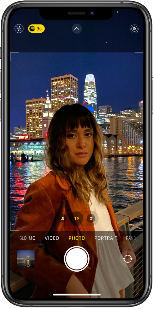 The Camera screen in Photo mode. Buttons for flash and Night mode appear in the top-left corner of the screen. The flash is turned off, and Night mode is on. The Camera Controls button is in top-center, and the Live Photo button is in the top-right corner. At the bottom of the screen are, from left to right, the Photo and Video Viewer button, the Take Picture button, and the Camera Chooser Back-Facing button.