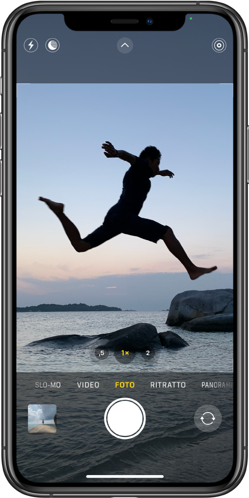 Schermata di Fotocamera in modalità Foto, con altre modalità a sinistra e a destra sotto il visore. I pulsanti per Flash, Modalità notturna, i controlli della fotocamera e Live Photo mostrati nella parte superiore dello schermo. Sotto le modalità della fotocamera sono visibili, da sinistra a destra, il pulsante per visualizzare le foto e i video, il pulsante di scatto e il selettore per la fotocamera posteriore.
