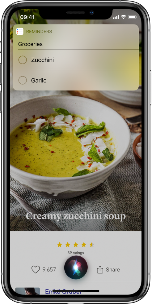 Em resposta ao pedido “Add zucchini and garlic to my groceries list”, Siri apresenta uma lista de lembretes designada Compras com curgetes e alho listadas. A lista aparece por cima de uma receita para sopa de curgetes.