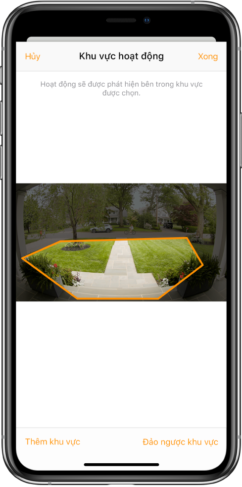 Màn hình iPhone đang hiển thị một vùng hoạt động bên trong hình ảnh được chụp bởi camera chuông cửa. Vùng hoạt động bao quanh phần sân phía trước và lối đi bộ, nhưng không bao gồm đường phố và đường lái xe. Các nút Hủy và Xong ở phía trên hình ảnh. Các nút Thêm vùng và Đảo ngược vùng ở bên dưới.