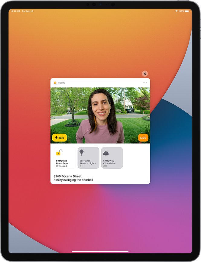 A notification from Home on the iPad screen. It shows the picture of a person at the front door with a Talk button at the left. Below are accessory buttons for the front door and entryway lights. The home’s address along with the words “Ashley is ringing the doorbell” appear under the accessory buttons. A Close button is at the top right of the notification.