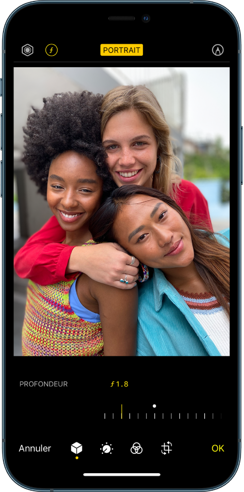 L’écran Modifier d’une photo prise en mode Portrait. En haut à gauche de l’écran se trouvent les boutons « Intensité de l’éclairage » et « Réglage de la profondeur ». En haut, au centre de l’écran, le bouton Portrait est activé et en haut à droite se trouve le bouton Modules. La photo est au centre de l’écran ; sous celle-ci se trouve un curseur permettant d’ajuster le réglage de la profondeur. Sous ce curseur se trouvent, de gauche à droite, les boutons Annuler, Portrait, Ajuster, Filtres, Recadrer et OK.