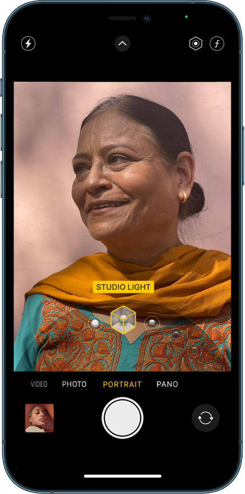 The Camera screen in Portrait mode; in the view finder, the subject is sharp and the background is blurred. The dial to select Portrait lighting effects is open in the bottom of the frame and Studio Light is selected. At the top left of the screen is the Flash button, at the top center is the Camera Controls button, and at the top right of the screen are the buttons to adjust Portrait lighting intensity and depth control. At the bottom of the screen are, from left to right, the Photo and Video Viewer button, the Take Picture button, and the Camera Chooser Back-Facing button.