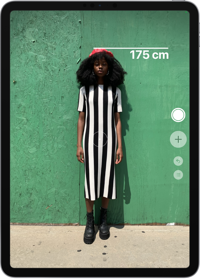 正在测量一个人的身高，身高测量结果显示在此人的头顶。右侧边缘的“拍照”按钮处于活跃状态，可用于拍摄测量结果的照片。绿色的“摄像头使用中”指示器显示在右上方。