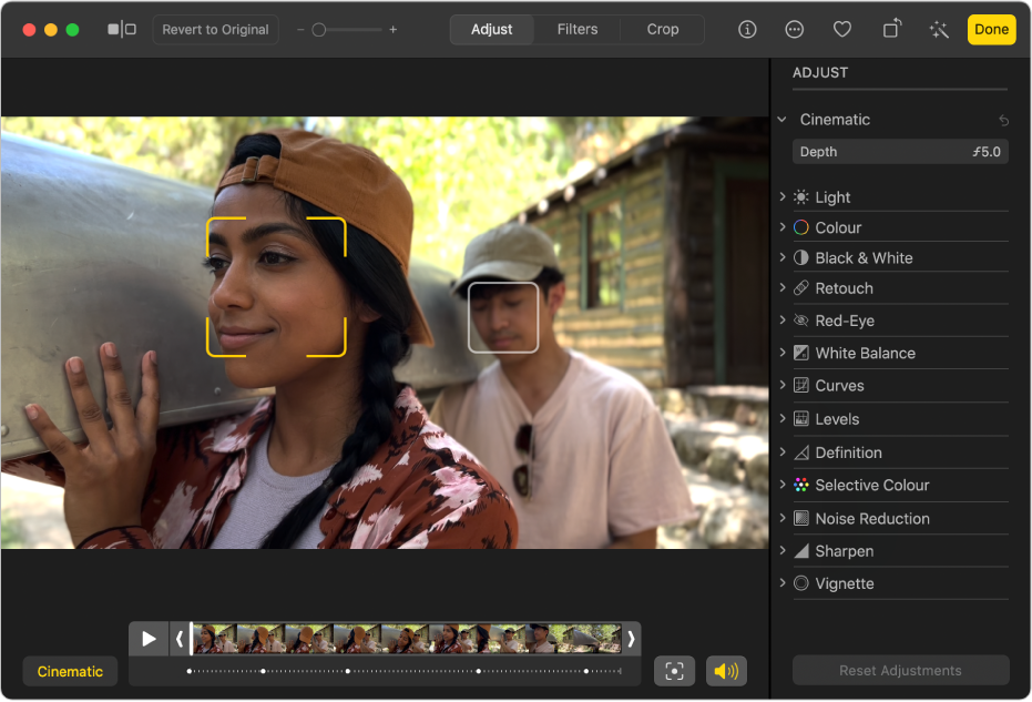 A video in editing view with a frame viewer below. A yellow box around a person’s face on the screen shows the subject currently in focus; a grey box shows another possible subject. The Cinematic button and Play button are to the left of the frame viewer, and the Toggle Focus button and Audio button are on the right. The Adjust pane is open on the right showing adjustment options.