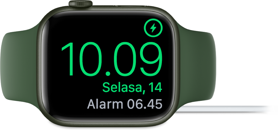Apple Watch diletakkan di sampingnya dan tersambung ke pengisi daya, dengan layar menampilkan simbol pengisian daya di pojok kanan atas, waktu saat ini di bawahnya, dan waktu alarm berikutnya.