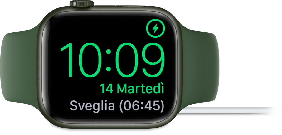Apple Watch appoggiato su un lato e collegato al caricabatterie, con lo schermo che mostra il simbolo di ricarica nell’angolo superiore destro, l’ora attuale sotto e l'orario della prossima sveglia.