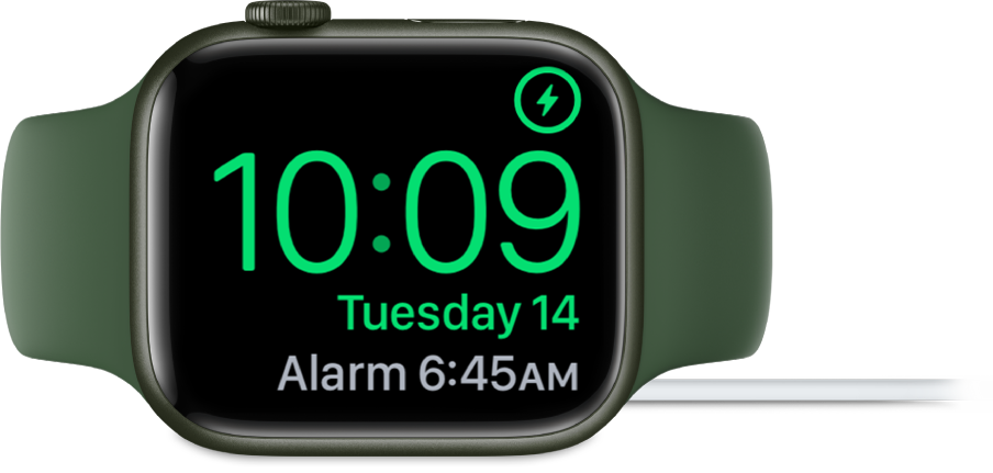 Ura Apple Watch na boku, priklopljena na polnilnik, na zaslonu pa je prikazan simbol za polnjenje v zgornjem levem kotu, trenutni čas pod njim in čas naslednjega alarma.