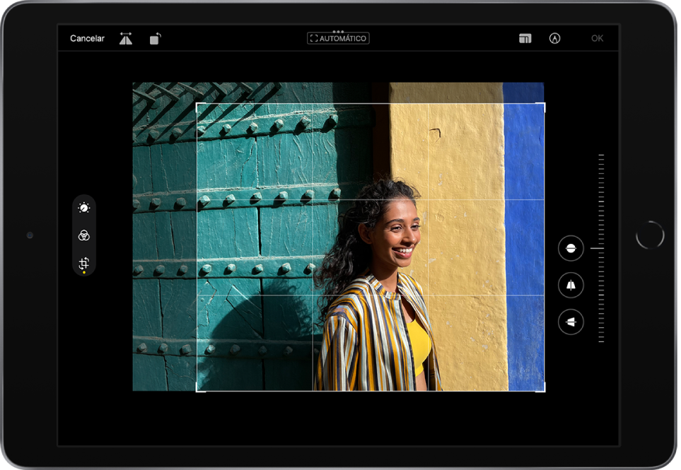 iPad en orientación horizontal. En el centro de la pantalla hay una foto en modo de edición con una superposición de cuadrícula y un marco de recorte. En la parte izquierda de la pantalla están los botones Ajustar, Filtros y Recortar; el botón Recortar está seleccionado. En el lado derecho de la pantalla están las opciones para mejorar el recorte y el regulador de intensidad. En la esquina superior izquierda están los botones Cancelar, Voltear y Girar. En la esquina superior derecha están los botones Proporciones, Marcación y OK.