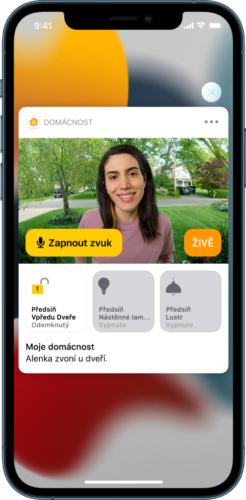 Displej iPhonu s oznámením od aplikace Domácnost. Zobrazuje se na něm snímek člověka u vstupních dveří s tlačítkem „Zapnout zvuk“ po levé straně. Pod ním se nacházejí tlačítka příslušenství pro osvětlení vstupních dveří a předsíně. Text zní: „Ashley zvoní u dveří.“ V pravém horním rohu oznámení se nachází tlačítko Zavřít.